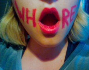 the word whore written on girls face with red lipstick